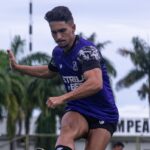 a man in a purple shirt and shorts running with his hand up